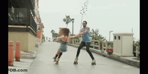 A Man And A Woman Rollerblading On A Sidewalk With The Man Holding The Woman 'S Hand GIF