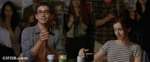 A Man And A Woman Sit At A Table Applauding In Front Of A Crowd GIF