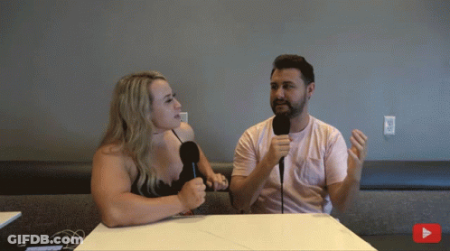 A Man And A Woman Sit At A Table With Microphones GIF