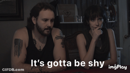 A Man And A Woman Sit At A Table With The Words It 'S Gotta Be Shy GIF