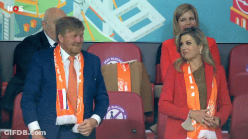 A Man And A Woman Sit In A Stadium With Seat Blocks Written On The Backs Of Their Seats GIF