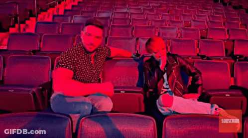 A Man And A Woman Sit In An Empty Auditorium With The Words Buc-Ee 'S GIF