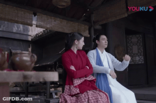 A Man And A Woman Sit Next To Each Other In Front Of A Youku Logo GIF