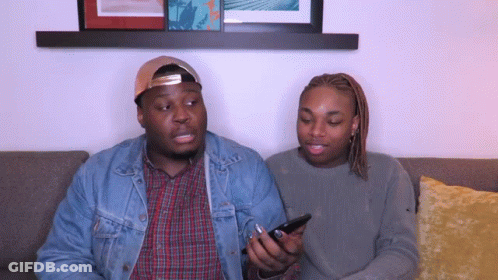 A Man And A Woman Sit On A Couch Looking At Their Phones GIF