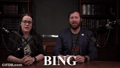 A Man And A Woman Sitting In Front Of A Microphone With A Sign That Says 80 % Bing GIF
