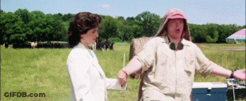 A Man And A Woman Standing In A Field With A Blue Cooler In The Foreground GIF