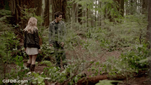 A Man And A Woman Standing In A Forest GIF