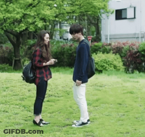 A Man And A Woman Standing Next To Each Other In A Park . GIF