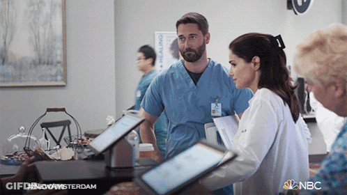 A Man And A Woman Standing Next To Each Other In A Room With Nbc Written In The Corner GIF