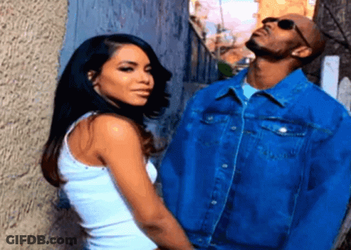 A Man And A Woman Standing Next To Each Other In Front Of A Wall GIF