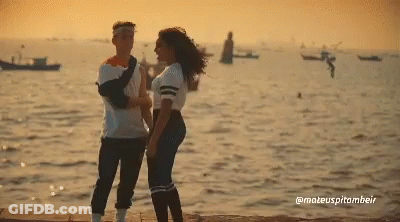 A Man And A Woman Standing Next To Each Other In Front Of The Ocean GIF