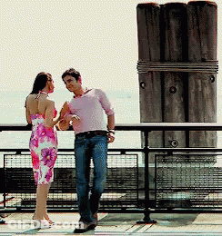 A Man And A Woman Standing Next To Each Other On A Balcony GIF