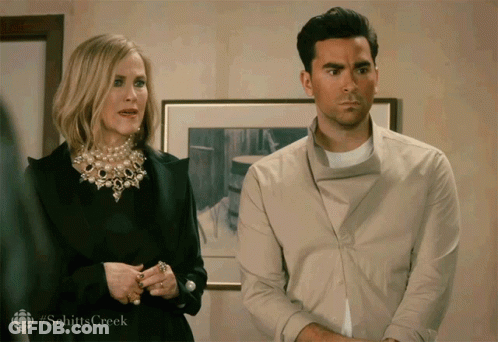 A Man And A Woman Standing Next To Each Other With #Schittscreek Written On The Bottom Right GIF