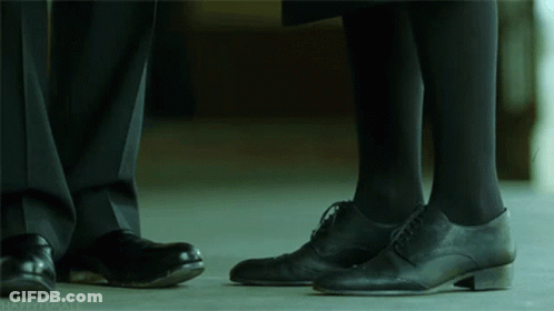 A Man And A Woman Standing Next To Each Other With Their Feet Touching GIF
