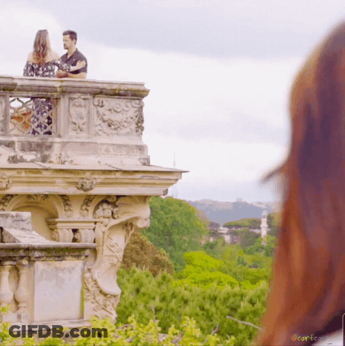 A Man And A Woman Standing On A Balcony Overlooking A Lush Green Forest With A Watermark That Says Corteco GIF