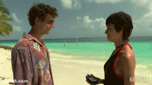 A Man And A Woman Standing On A Beach With Netflix Written On The Bottom GIF