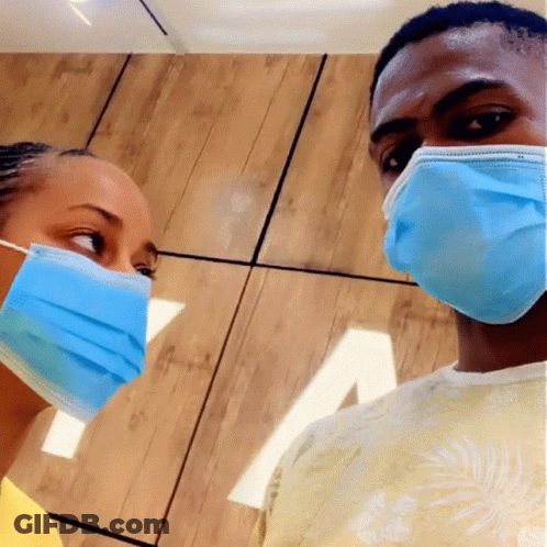 A Man And A Woman Wearing Blue Face Masks Looking At Each Other GIF