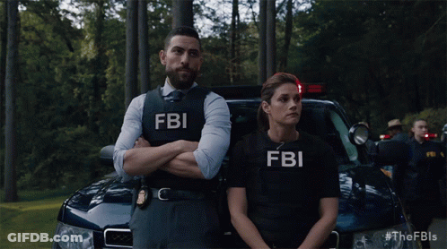 A Man And A Woman Wearing Fbi Vests Standing In Front Of A Car GIF
