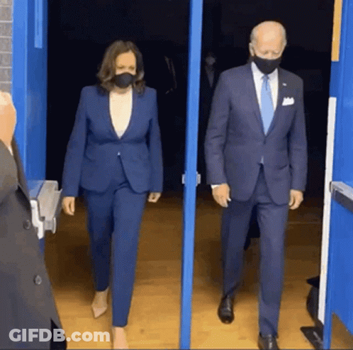 A Man And A Woman Wearing Masks Are Walking Out Of A Doorway . GIF
