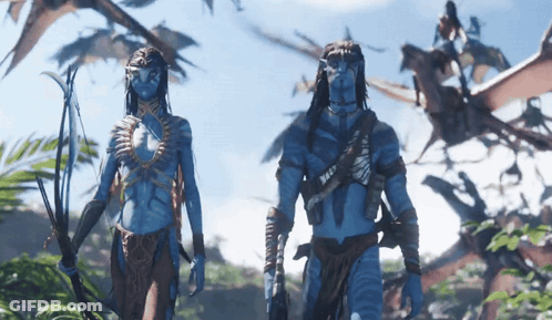 A Man And A Woman With Blue Faces Are Standing In A Forest GIF