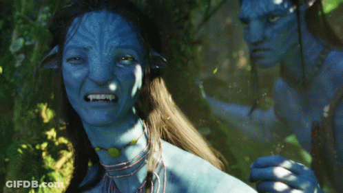 A Man And A Woman With Blue Faces Are Standing In A Forest GIF