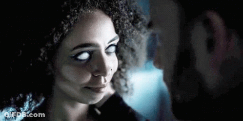 A Man And A Woman With White Eyes Are Looking At Each Other In A Dark Room . GIF