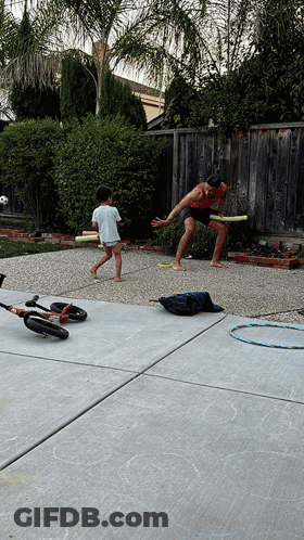 A Man And Child Are Playing Frisbee In A Backyard GIF