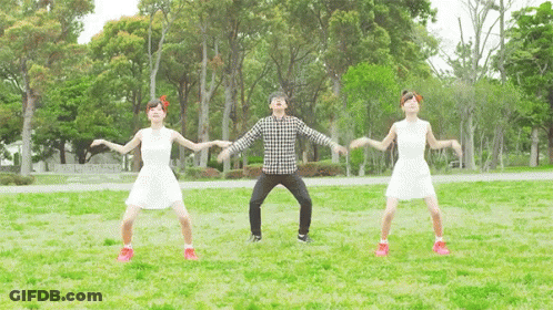 A Man And Two Women Are Dancing In A Park With Trees In The Background GIF