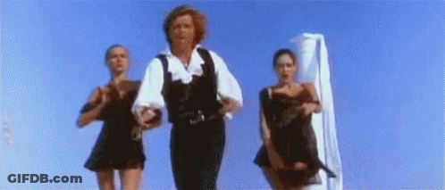 A Man And Two Women Are Dancing On A Beach In Front Of A Blue Sky . GIF