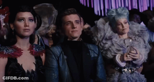 A Man And Two Women Are Sitting In A Crowd Looking At Something GIF