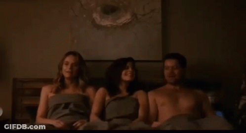 A Man And Two Women Are Sitting On A Bed Without Shirts . GIF