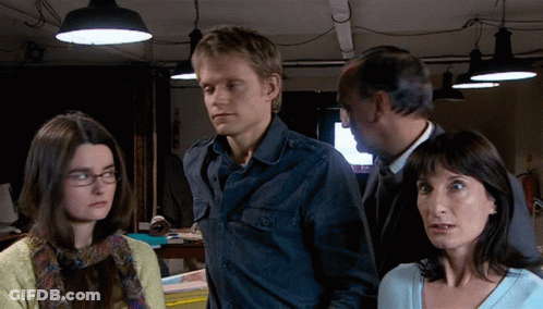 A Man And Two Women Are Standing In A Dark Room With Lamps Hanging From The Ceiling GIF