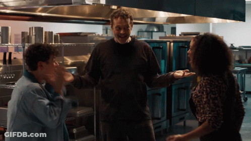 A Man And Two Women Are Standing In A Kitchen And The Man Is Smiling GIF
