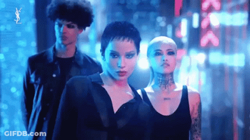 A Man And Two Women Are Standing Next To Each Other In A Dark Room With Neon Lights Behind Them . GIF
