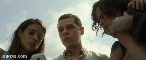 A Man And Two Women Look At A Cell Phone Together GIF