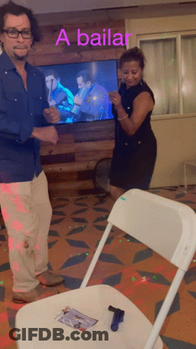 A Man And Woman Are Dancing In Front Of A Tv That Says A Bailar On It GIF