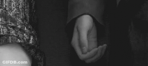 A Man And Woman Are Holding Hands In A Black And White Photo . GIF