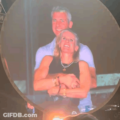 A Man And Woman Are Hugging Each Other In Front Of A Sign That Says M GIF