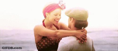 A Man And Woman Are Hugging Each Other On The Beach . GIF
