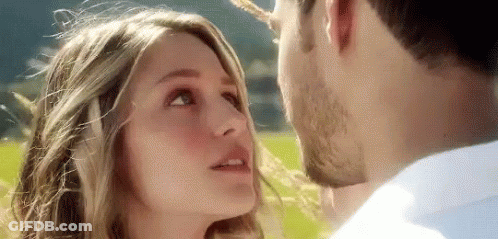 A Man And Woman Are Kissing In A Field . GIF