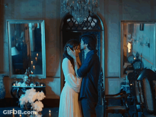A Man And Woman Are Kissing In A Room With Candles GIF