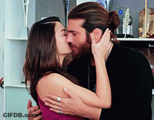 A Man And Woman Are Kissing In Front Of A Shelf With Trophies On It . GIF