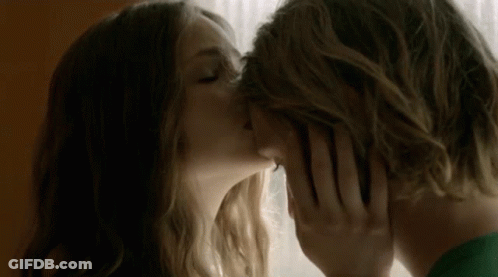 A Man And Woman Are Kissing In Front Of A Window . GIF