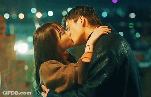 A Man And Woman Are Kissing In The Rain At Night GIF