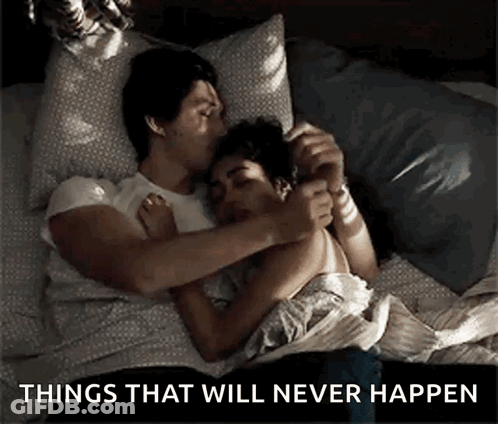 A Man And Woman Are Laying In Bed Hugging And Kissing . GIF