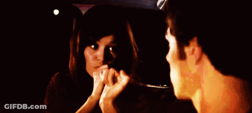 A Man And Woman Are Looking At Each Other In A Dark Room GIF