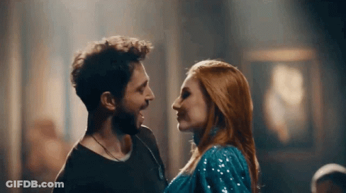 A Man And Woman Are Looking At Each Other In A Dark Room . GIF