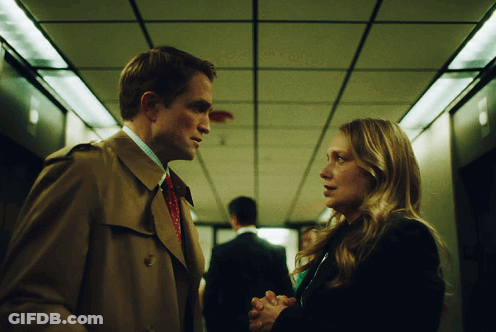 A Man And Woman Are Looking At Each Other In A Hallway GIF