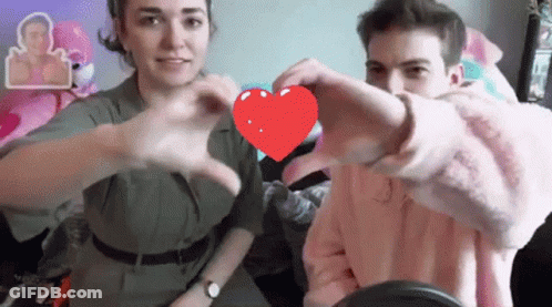 A Man And Woman Are Making A Heart Shape With Their Hands GIF