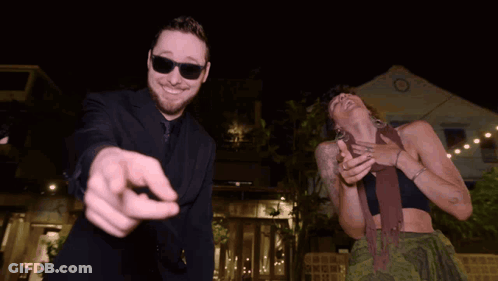 A Man And Woman Are Pointing At The Camera At Night GIF
